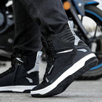 Person wearing black high-top sneakers with white soles on a motorcycle background