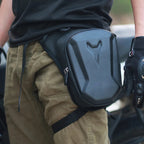 Person wearing a black backpack with a brand logo, holding a camera, on a blurred background.