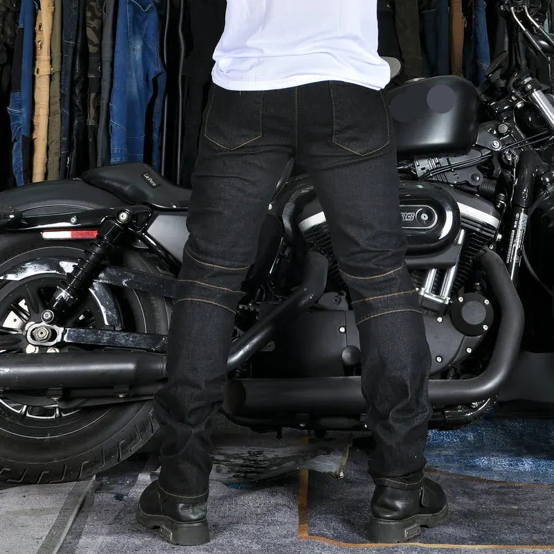 Person wearing black jeans and boots standing next to a Harley Davidson motorcycle in a garage.