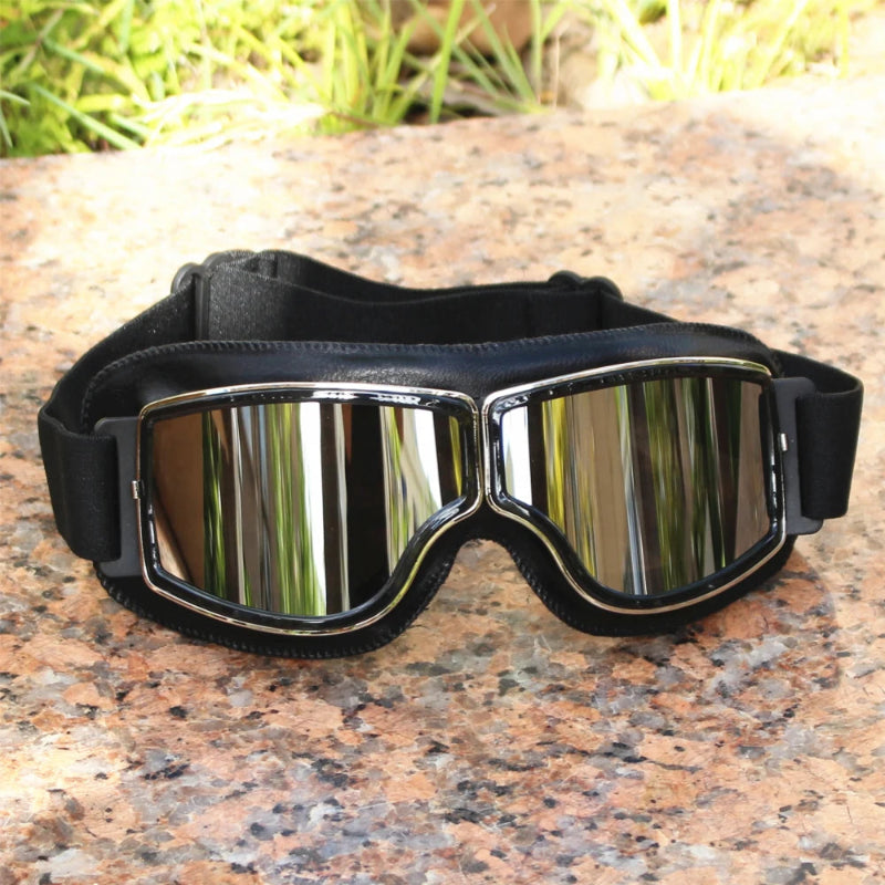 Black goggles with reflective lenses on a stone surface with grass in the background