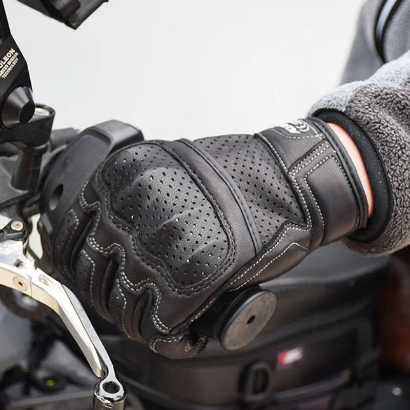 Person wearing a black motorcycle glove on a handlebar with a blurred background