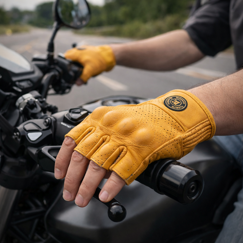 Yellow motorcycle glove on a gloved hand gripping a handlebar, with a blurred road and trees in the background.