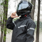 Person wearing a black raincoat and helmet on a motorcycle with trees in the background