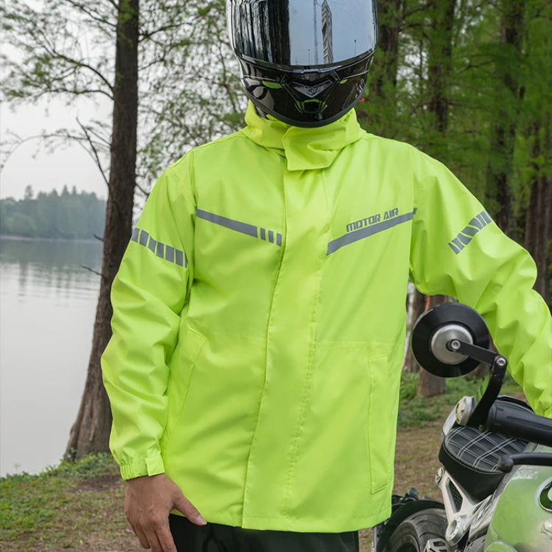 Person wearing a bright yellow motorcycle raincoat and helmet near a motorcycle by a lake.