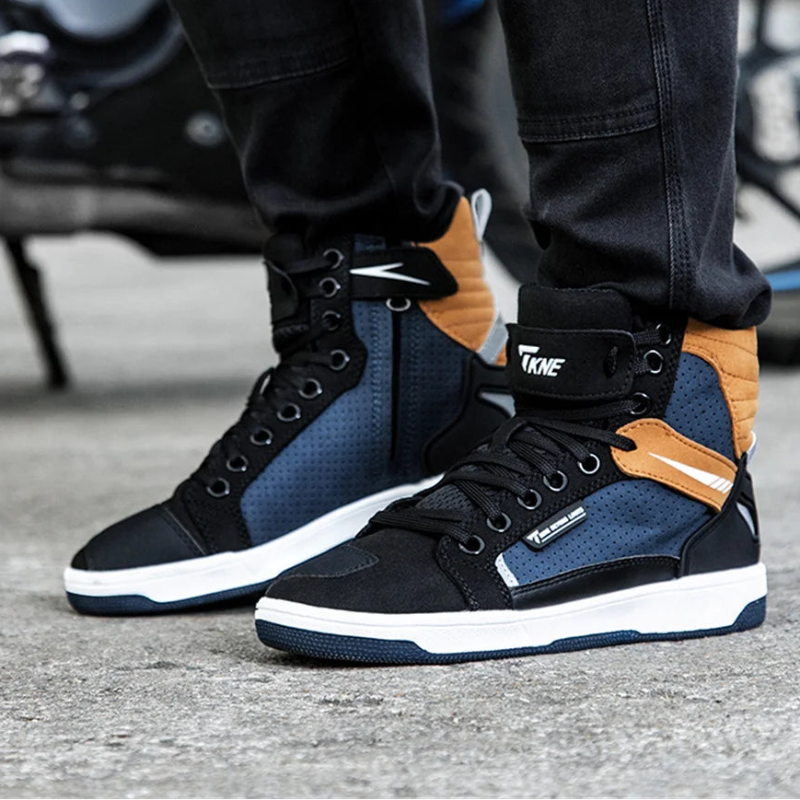 Black and blue sneakers with brown accents worn by a person, with a motorcycle in the background.